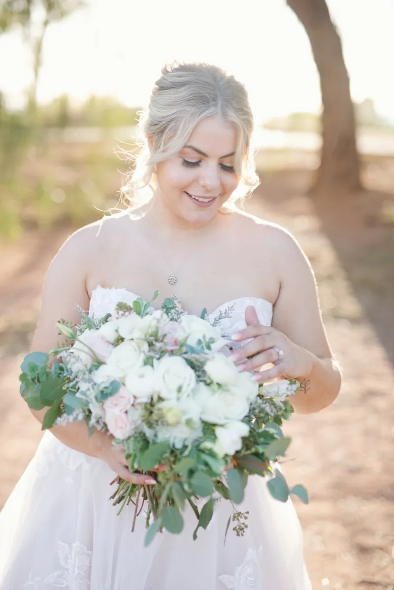 Bride looking down at a loose white and blush bouquet of roses and eucalyptus in her hands