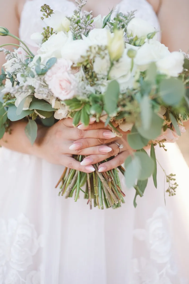 Close crop of the bride's hands holding the wrapped stems of her bouquet with her ring showing
