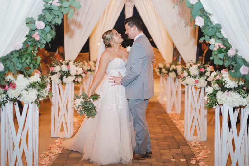 Couple holding each other at the flower lined aisle just after the ceremony, string lights glowing behind them