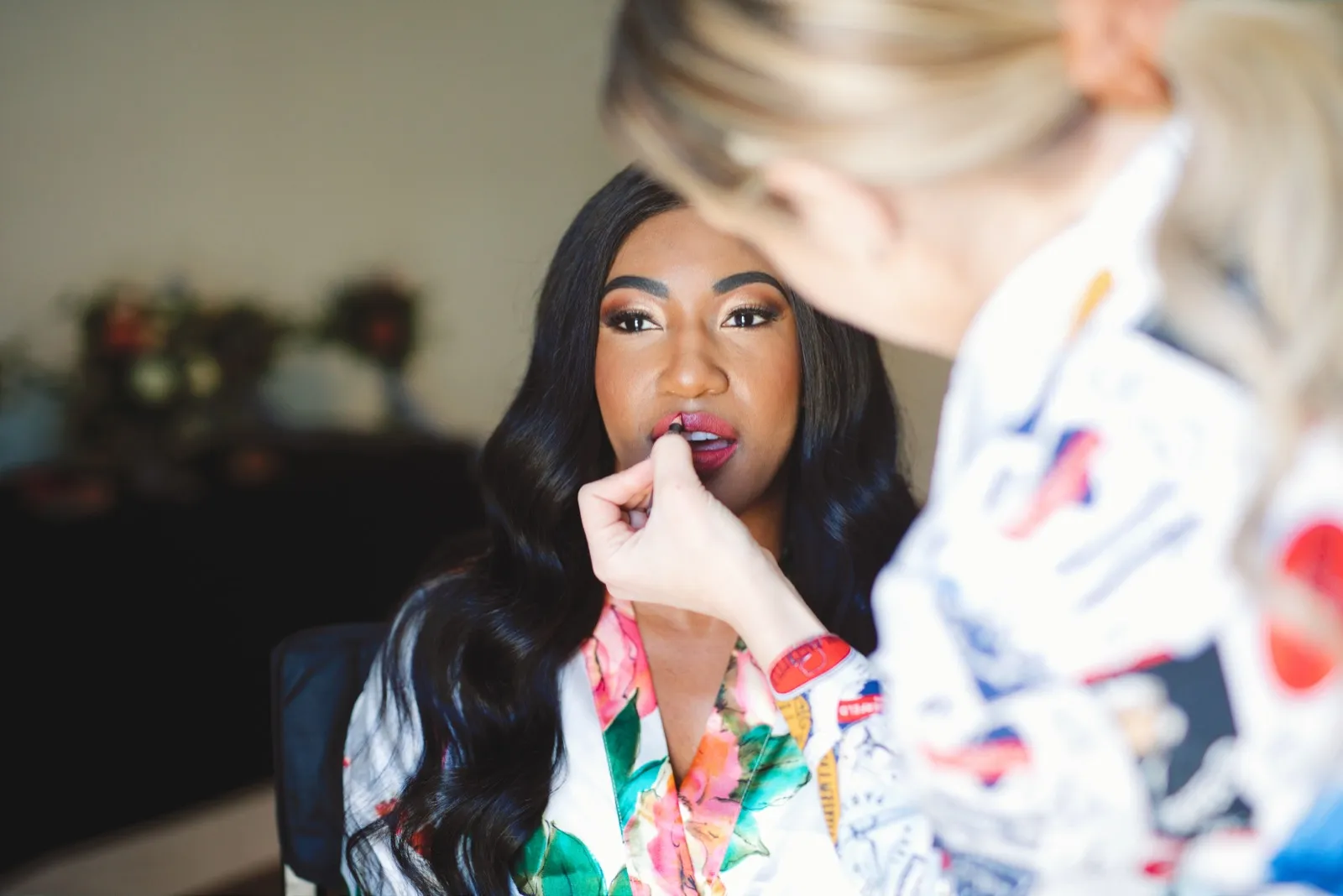 Makeup artist applying a bride’s lipstick as she sits in a floral robe before the ceremony