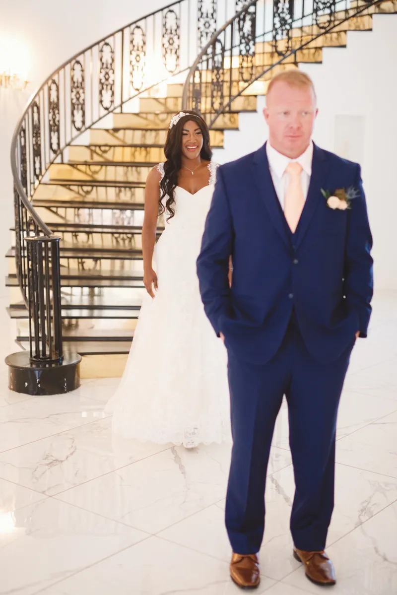 Bride and groom standing side by side at the bottom of one of the curved staircases, the groom in a blue suit with his hands in his pockets