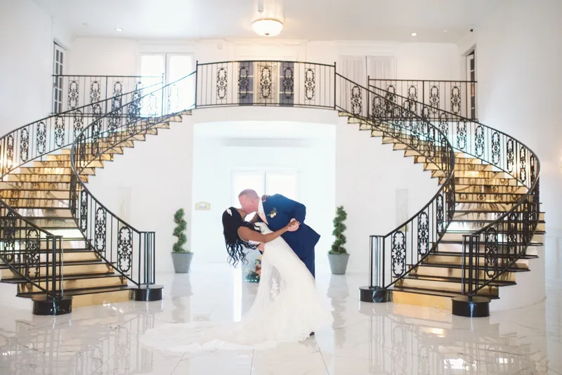Groom dipping the bride backward for a kiss in the middle of the entry hall with both staircases curving behind them