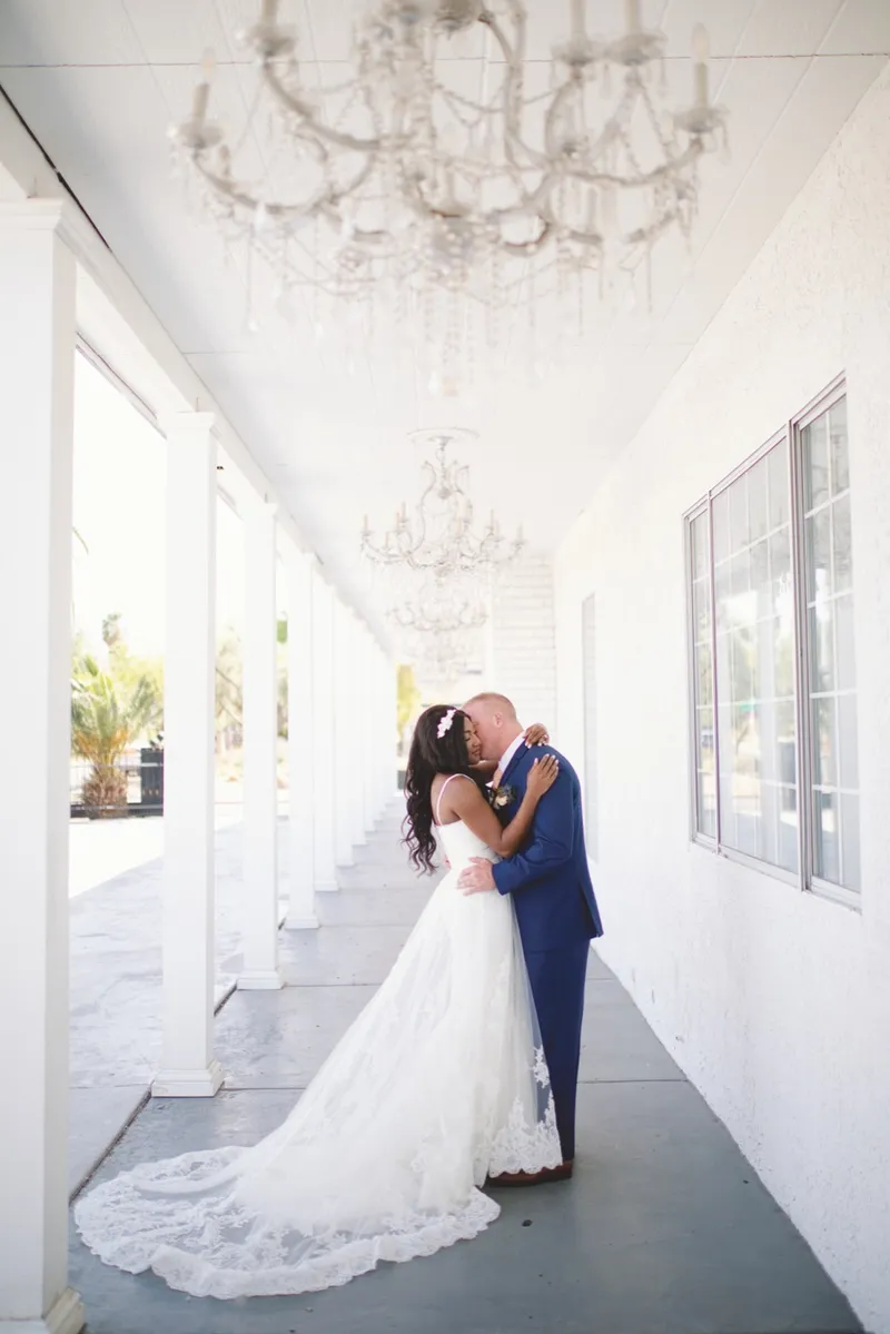 Couple holding each other in the covered walkway with the bride's train spread across the floor and chandeliers overhead