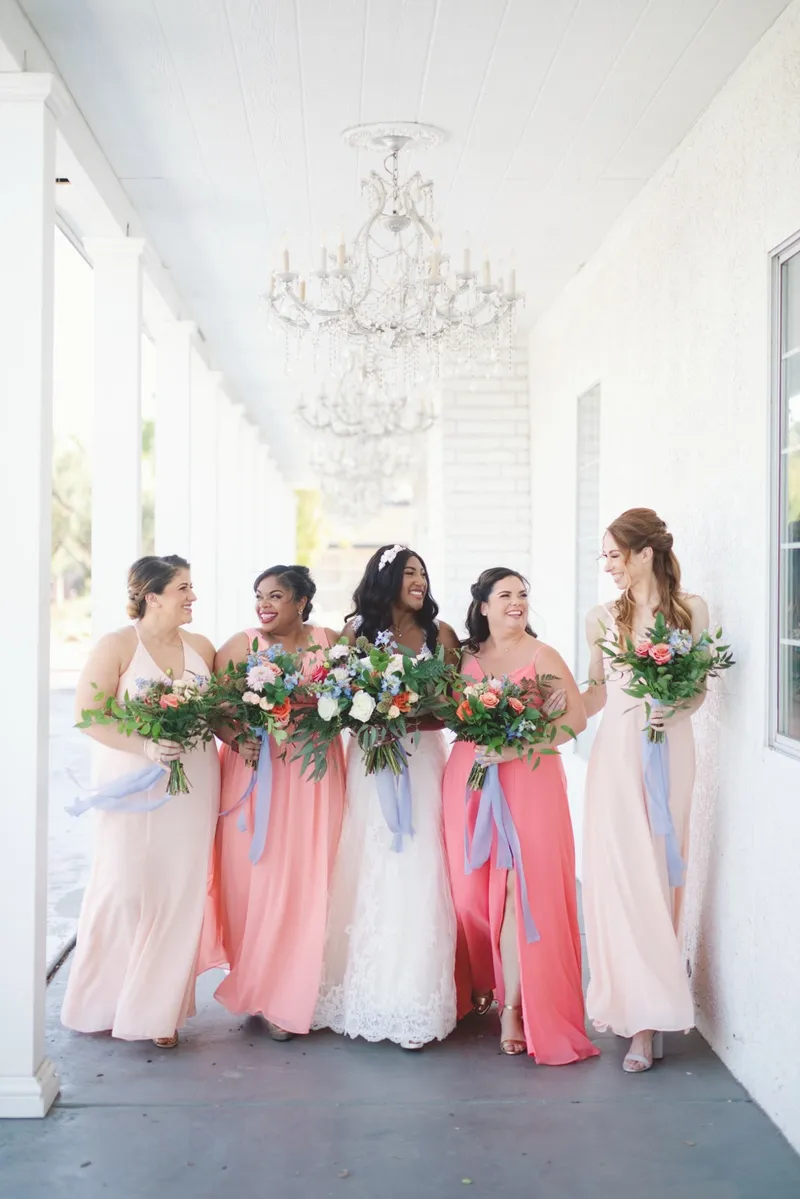 Bride and her bridesmaids walking side by side down the length of the covered walkway with their bouquets