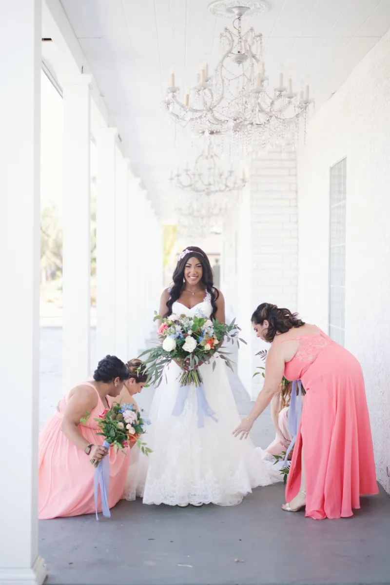 Two bridesmaids crouched down to spread the bride's lace train out along the floor of the walkway