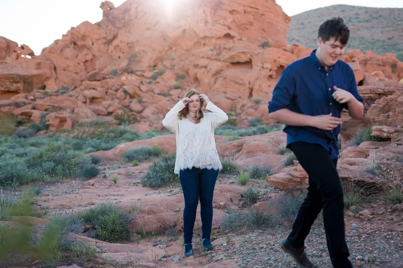 Woman smoothing her hair while her partner walks past her across the red rock