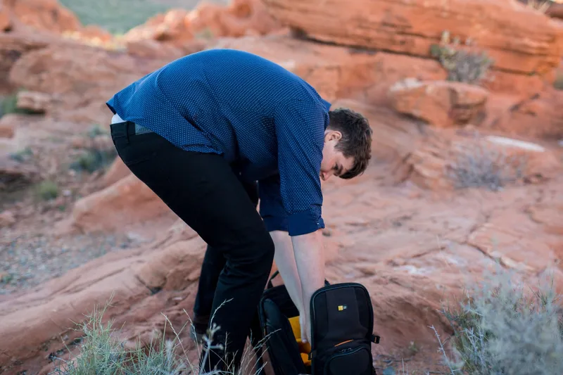 Man crouching over a backpack on the sandstone a moment before he asks