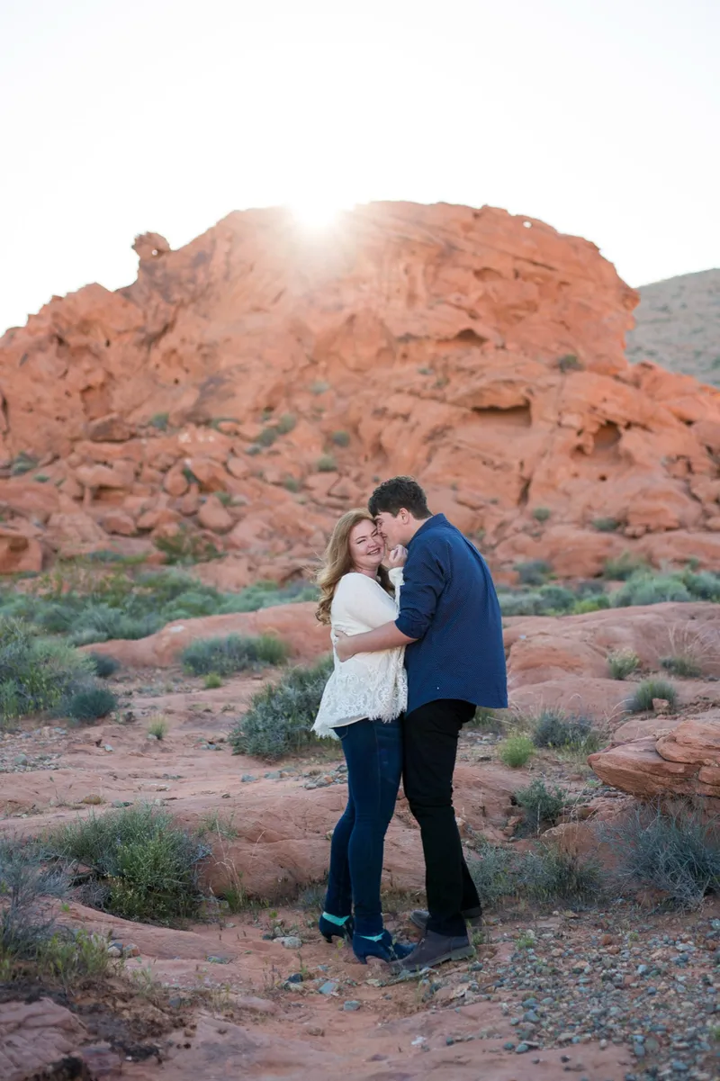 Newly engaged couple laughing into each other with the sun breaking over the red ridge
