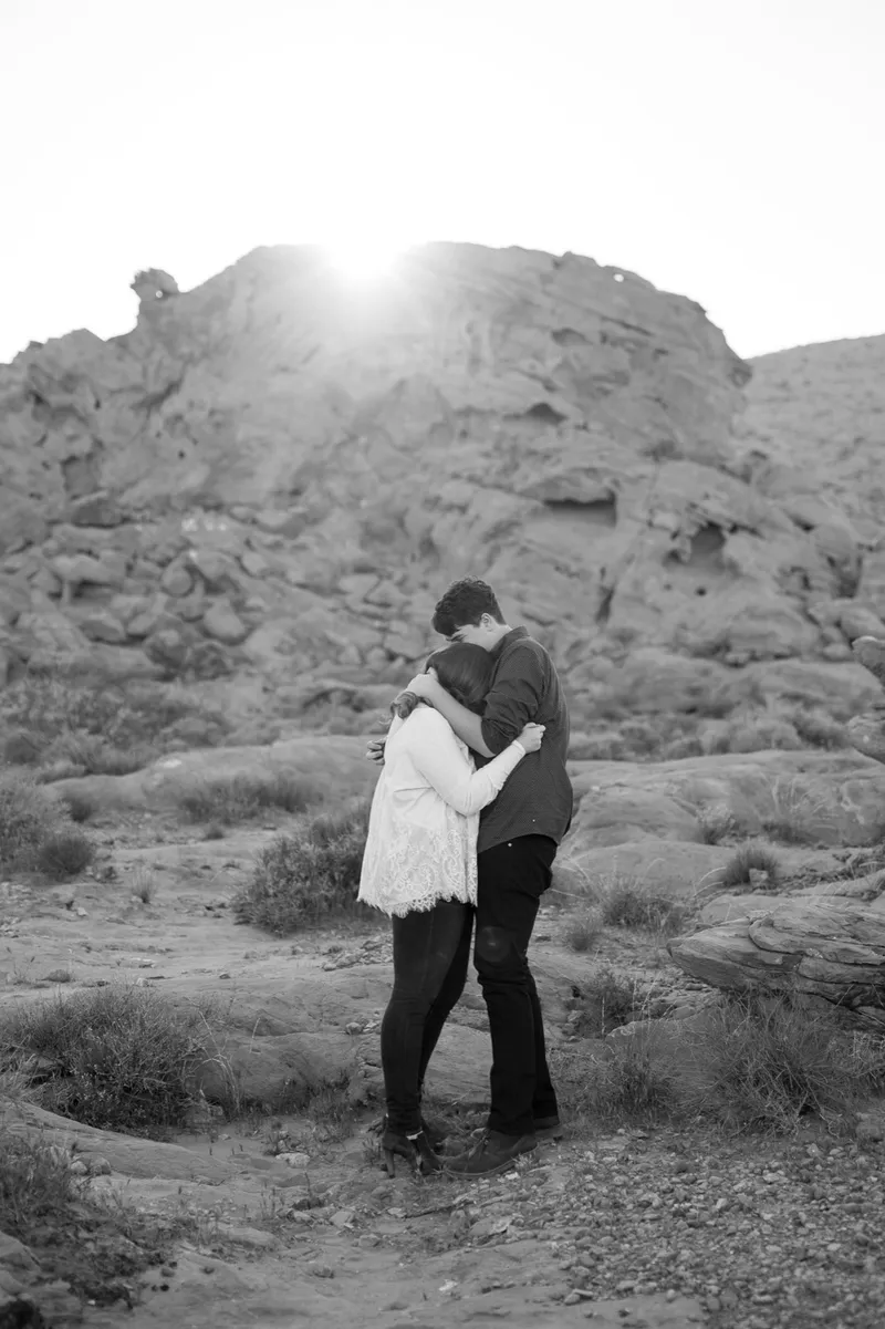 Black and white photo of the couple holding each other below the sandstone ridge