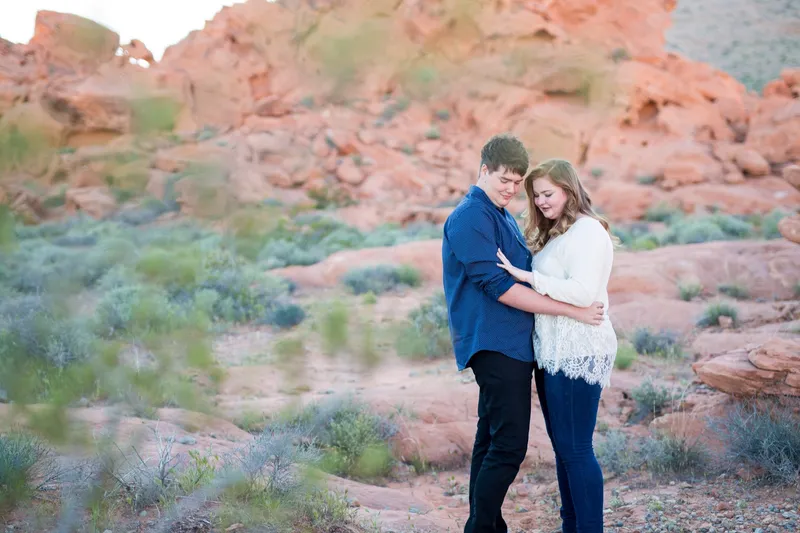 Couple standing together framed by green desert brush with orange rock behind them