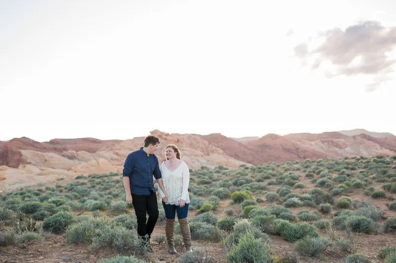 Newly engaged couple walking hand in hand through low sage with striped hills in the distance