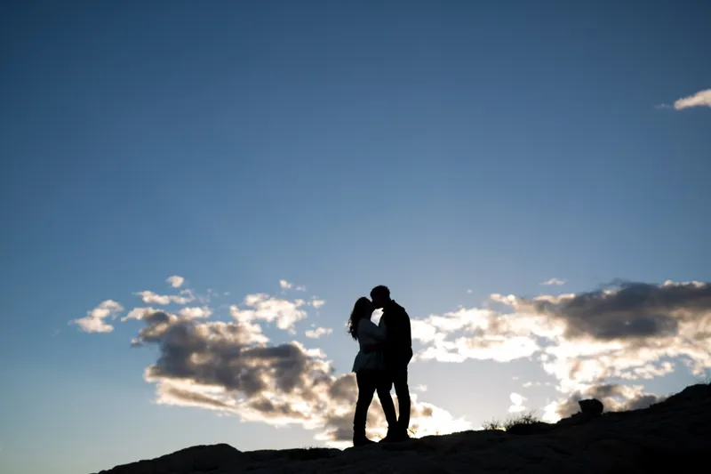 Silhouette of the two of them kissing on a ridge against a cloudy sunset sky