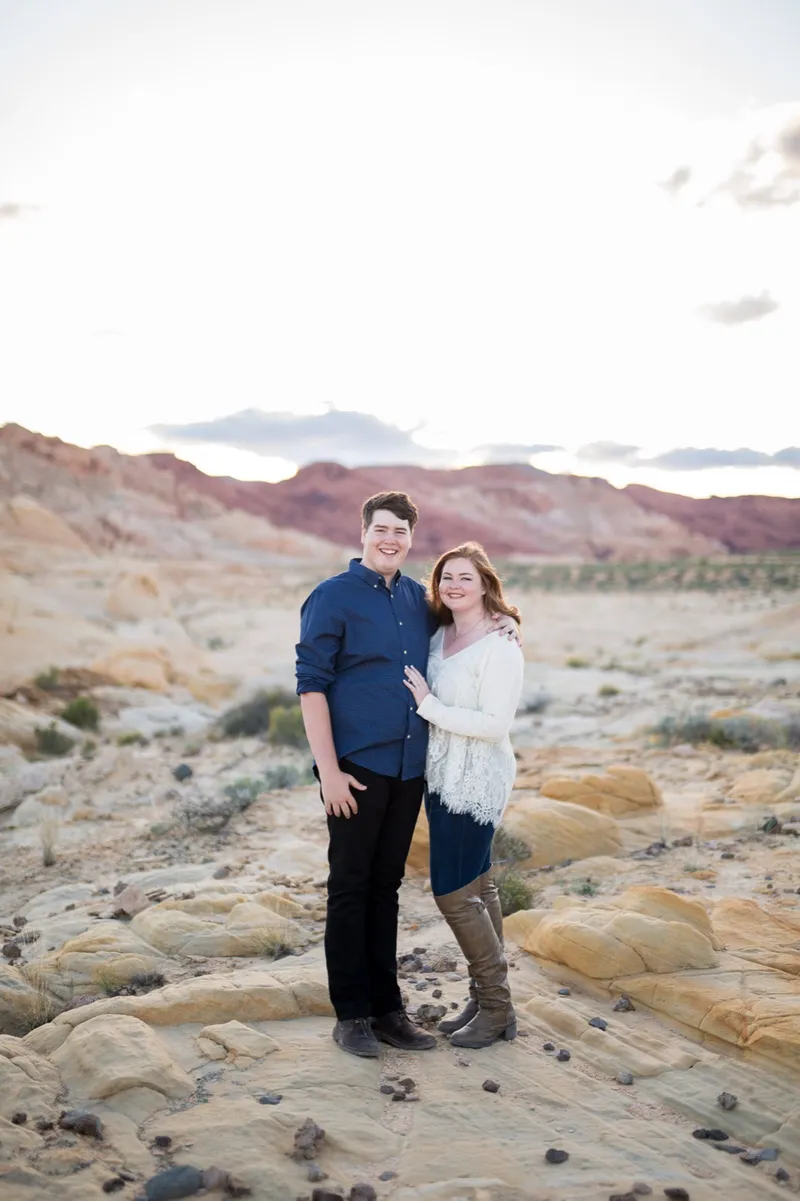 Couple standing on pale yellow sandstone with the pink and cream hills spread out behind them