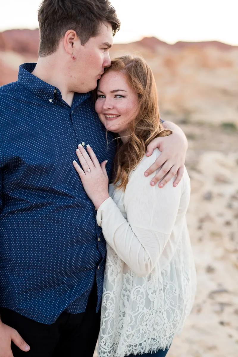 Close photo of her smiling with her hand on his chest as he kisses the top of her head